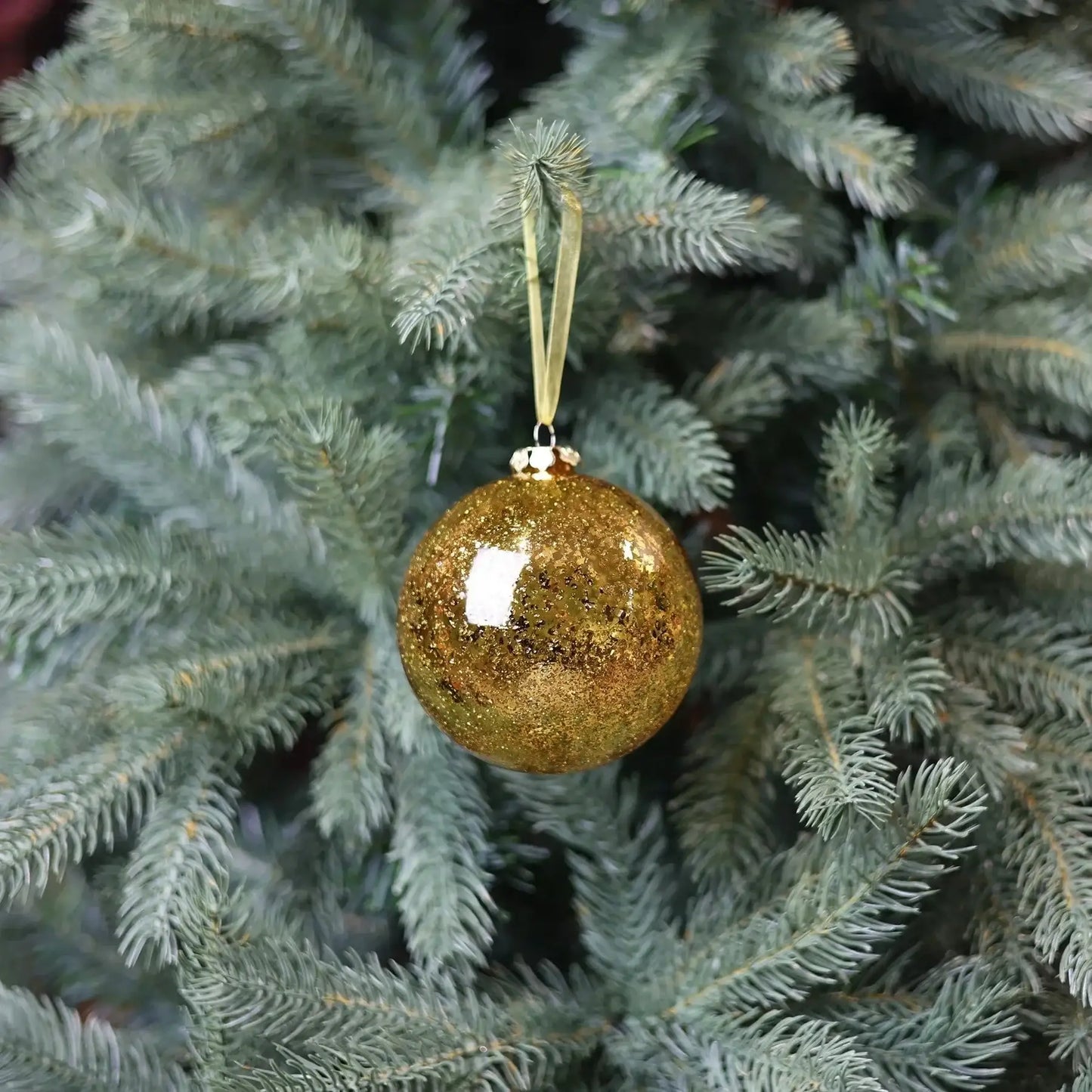 Gold glitter Christmas ornament hanging on a green tree branch, festive holiday decor
