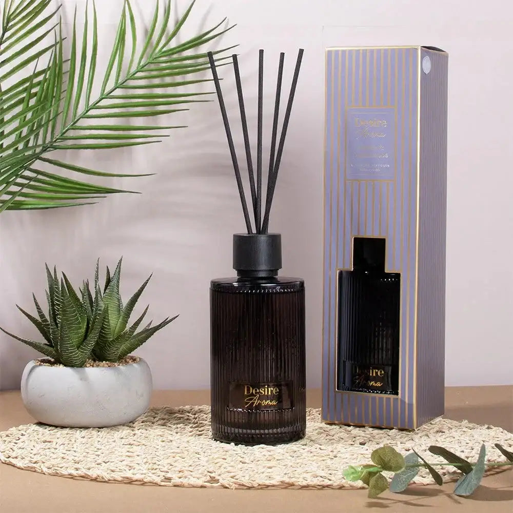 Black Desire Aroma reed diffuser with gift box, surrounded by plants on a woven mat