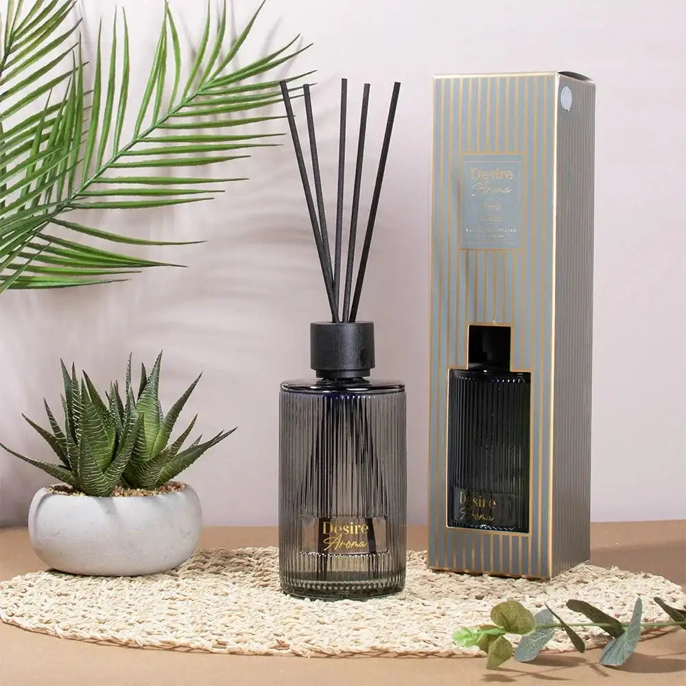 Reed diffuser gift set with striped glass bottle, box, and indoor plants on a woven mat.