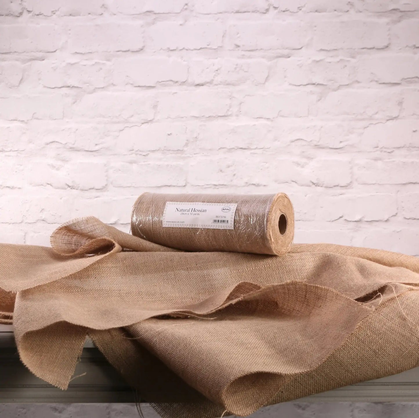 Natural hessian fabric roll for home décor and gift wrapping, rustic texture against white brick wall