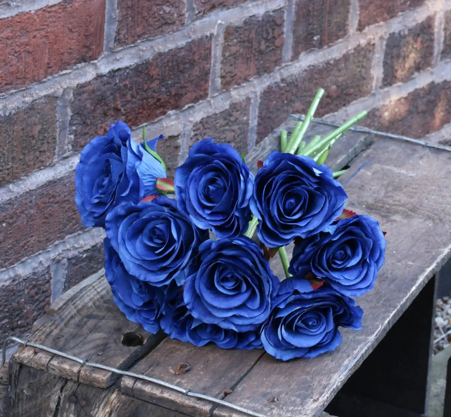 Deep blue artificial roses on rustic wood crate against brick wall, perfect for home décor or gift occasions
