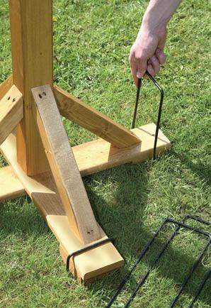 Hand securing wooden garden stake with metal hook on grass, ideal for outdoor décor and gifts