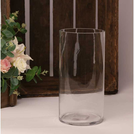 Clear glass cylinder vase on a table with floral décor and wooden crate backdrop