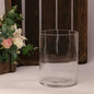 Clear glass cylinder vase for home décor, placed near pink and white artificial flowers.