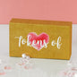 Gift box with pink heart graphic and 'tokens of' text, surrounded by clear gem decorations.