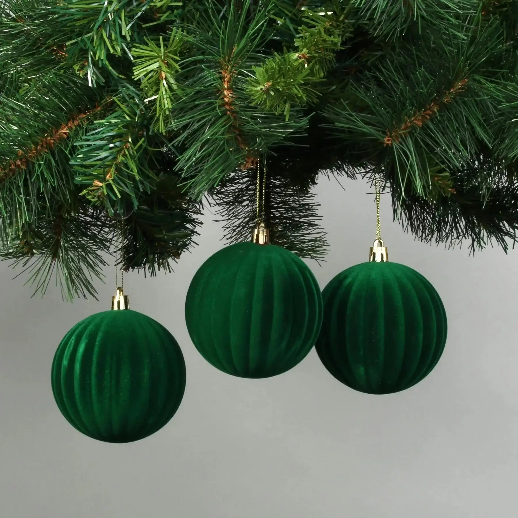 Emerald green velvet Christmas ornaments hanging on a tree branch, perfect for holiday home décor and festive celebrations.