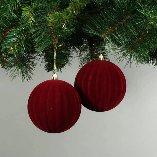 Red velvet Christmas baubles hanging on a green tree branch, festive holiday decor
