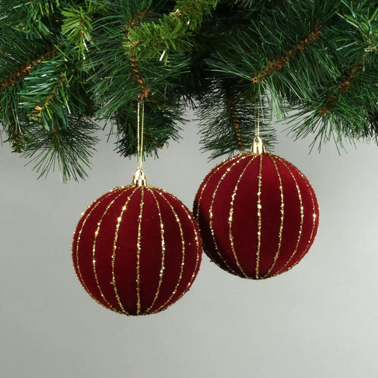 Red velvet Christmas ornaments with gold glitter stripes hanging on tree branches