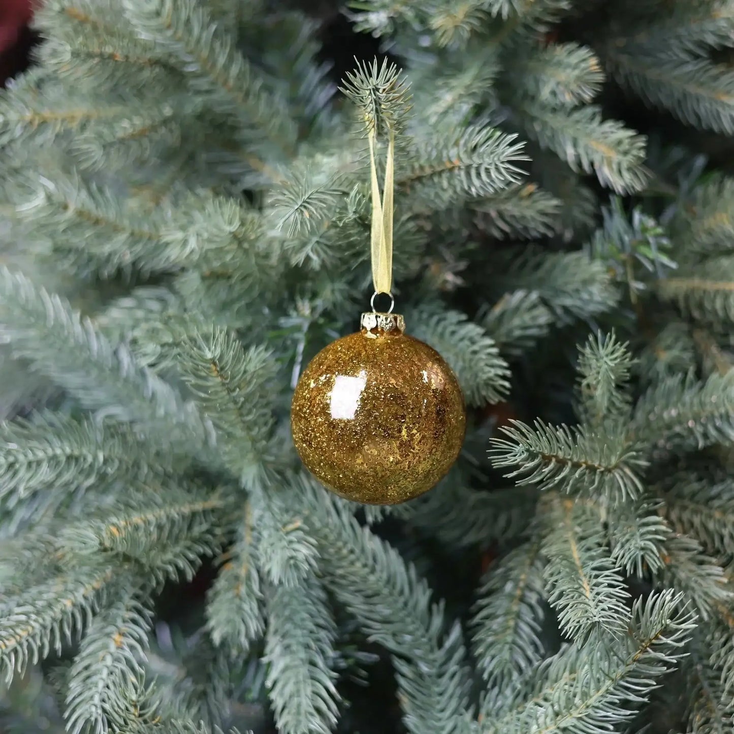 Gold glitter Christmas ornament hanging on a green pine tree branch
