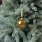Gold glitter Christmas ornament hanging on a green pine tree branch