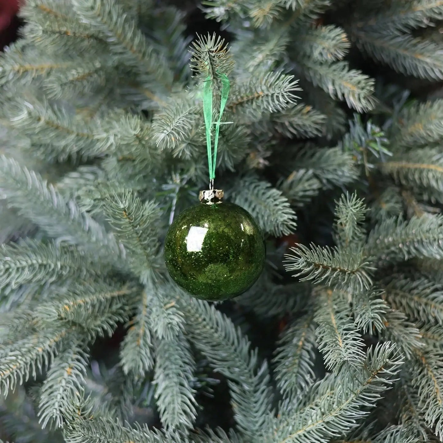 Green glass Christmas ornament hanging on a pine tree branch, festive holiday decor