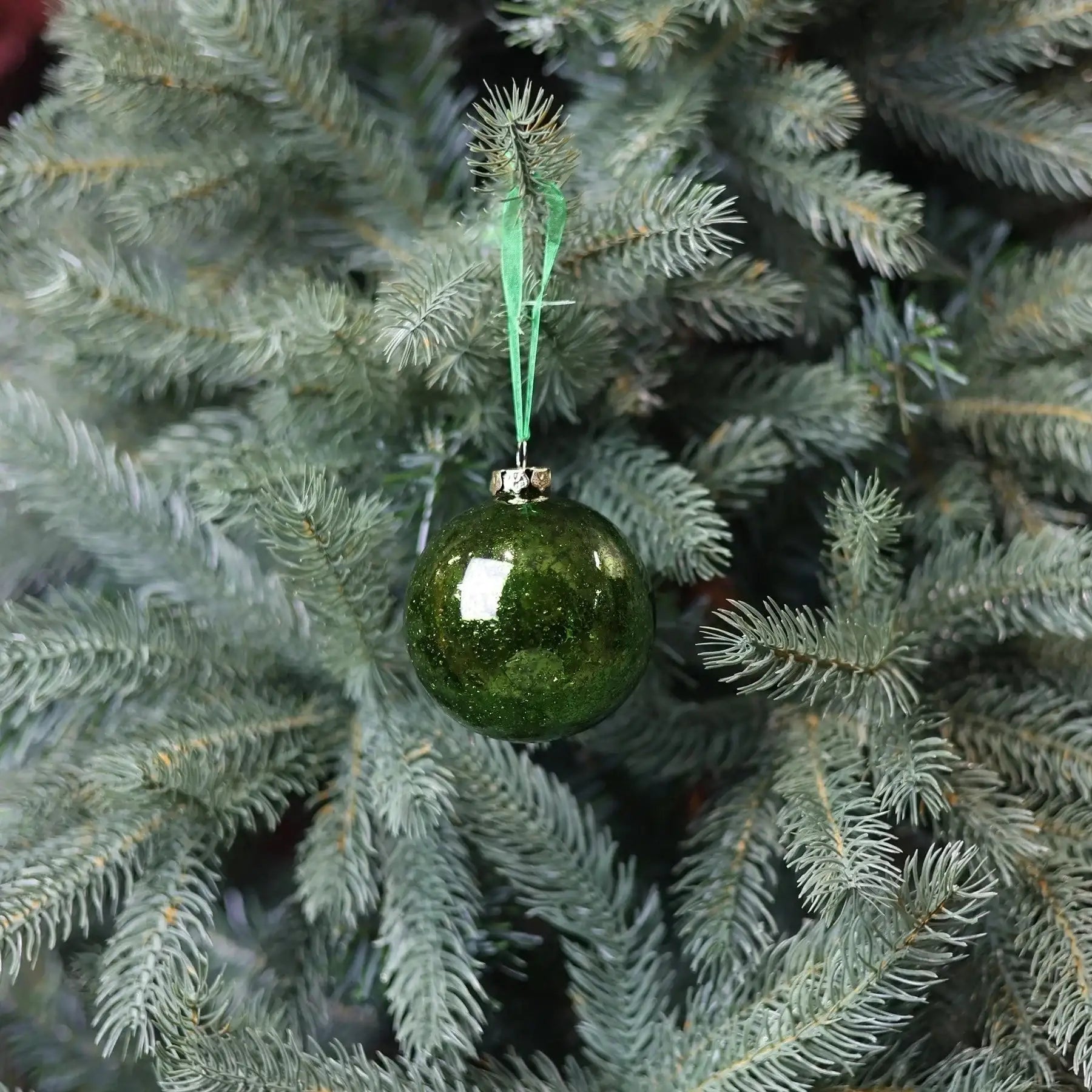 Green glass Christmas ornament hanging on a pine tree branch, festive holiday decor