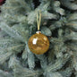 Gold glitter Christmas ornament hanging on a green tree branch, festive holiday decor