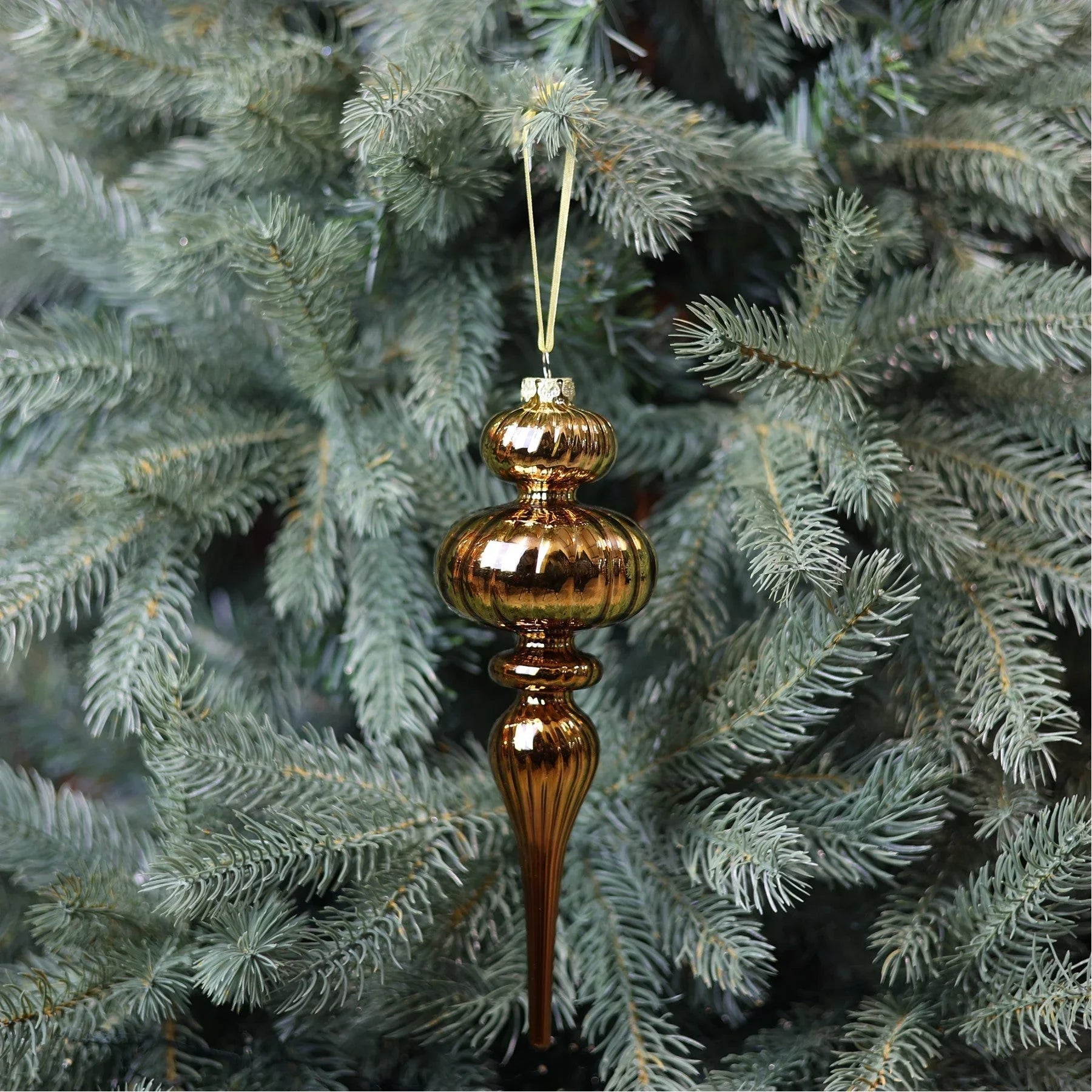 Vintage gold glass finial ornament hanging on a pine Christmas tree
