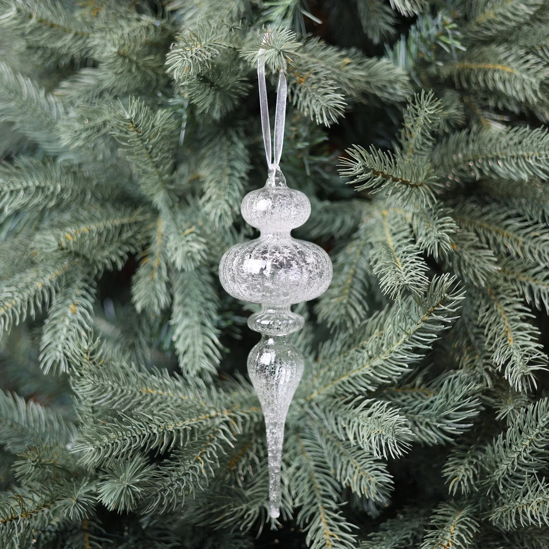 Clear glass icicle ornament hanging on a Christmas tree with green pine needles