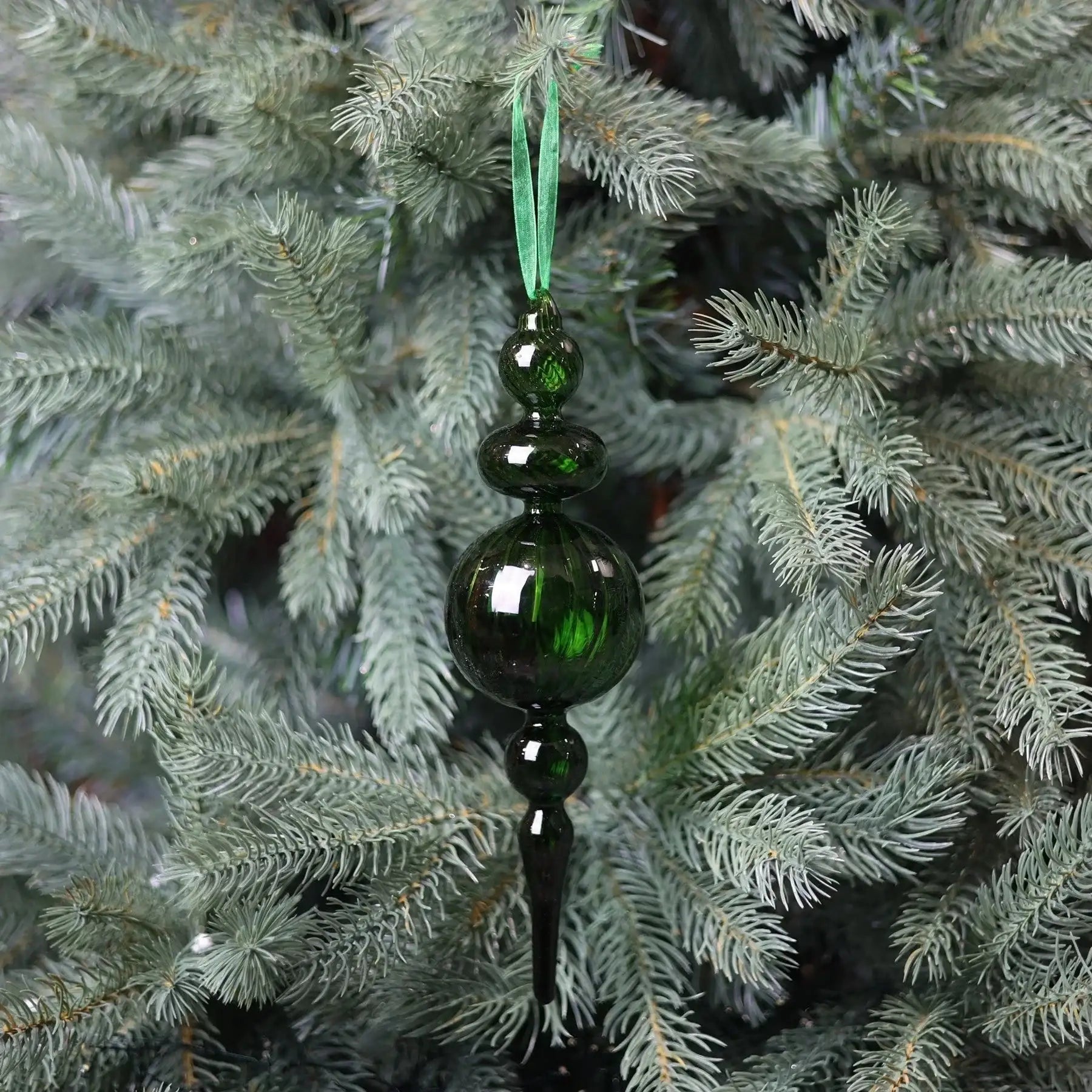 Green glass ornament hanging on a Christmas tree with silver pine needles