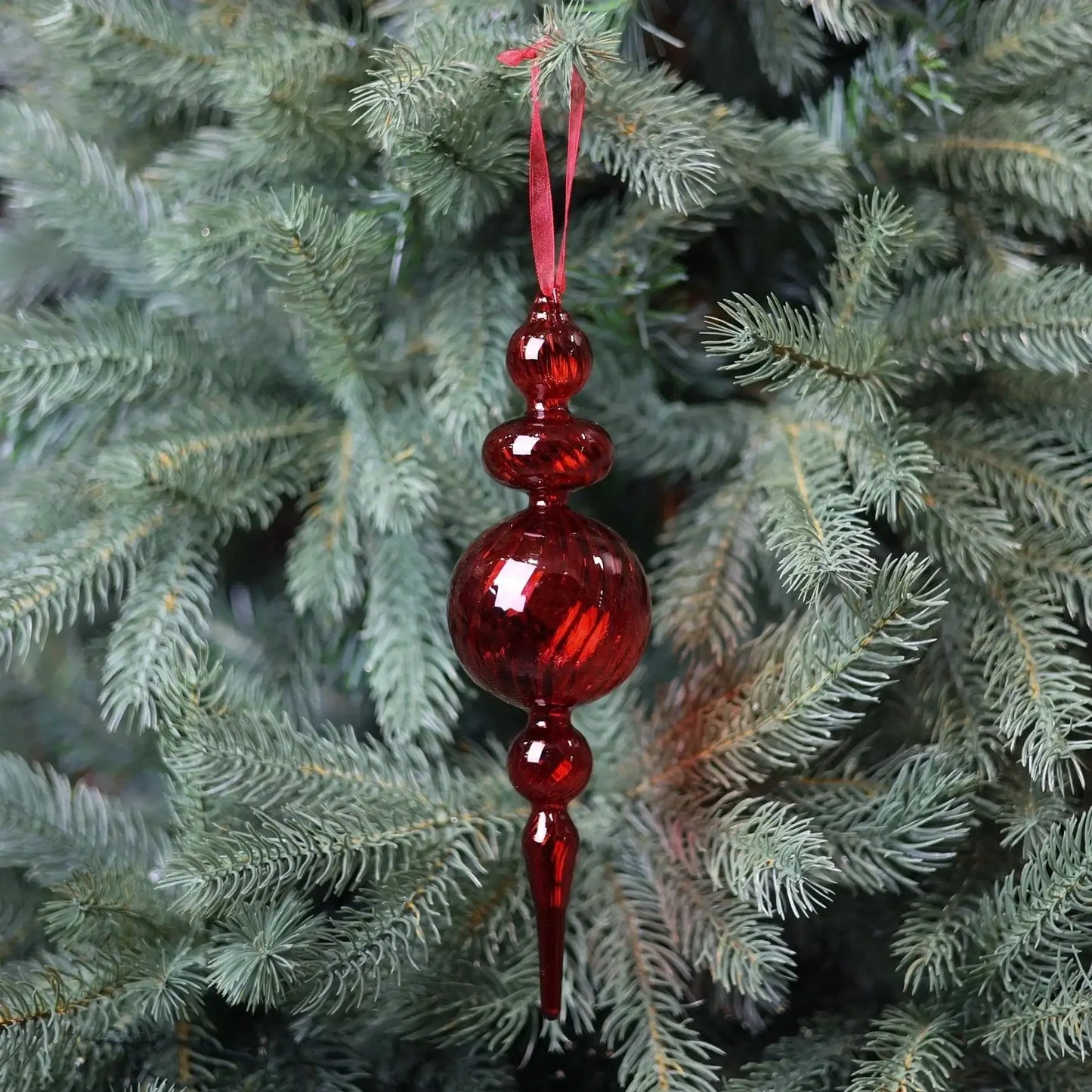 Red glass Christmas ornament hanging on pine tree, festive holiday decor