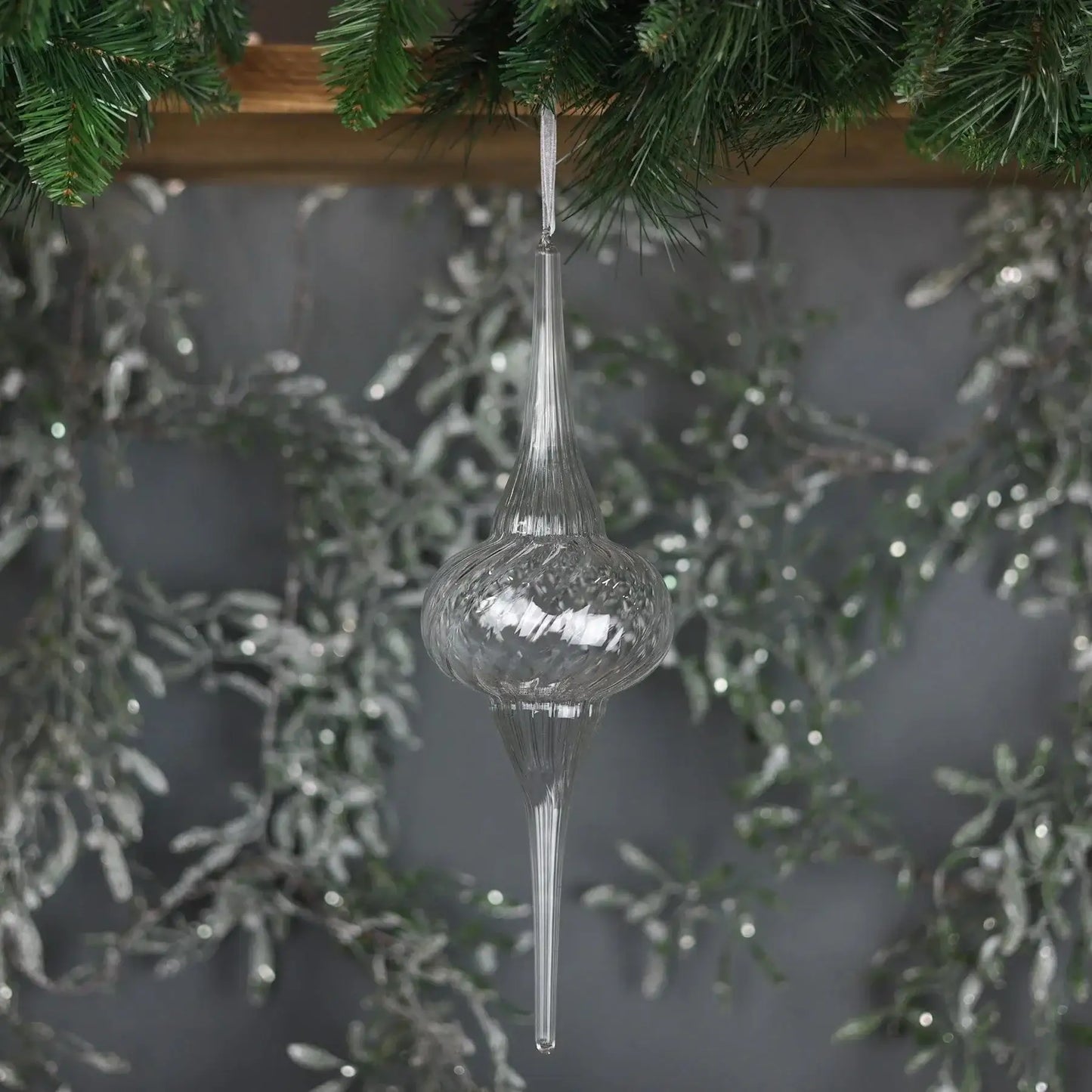 Clear glass Christmas tree ornament hanging from pine garland with silver holiday decor