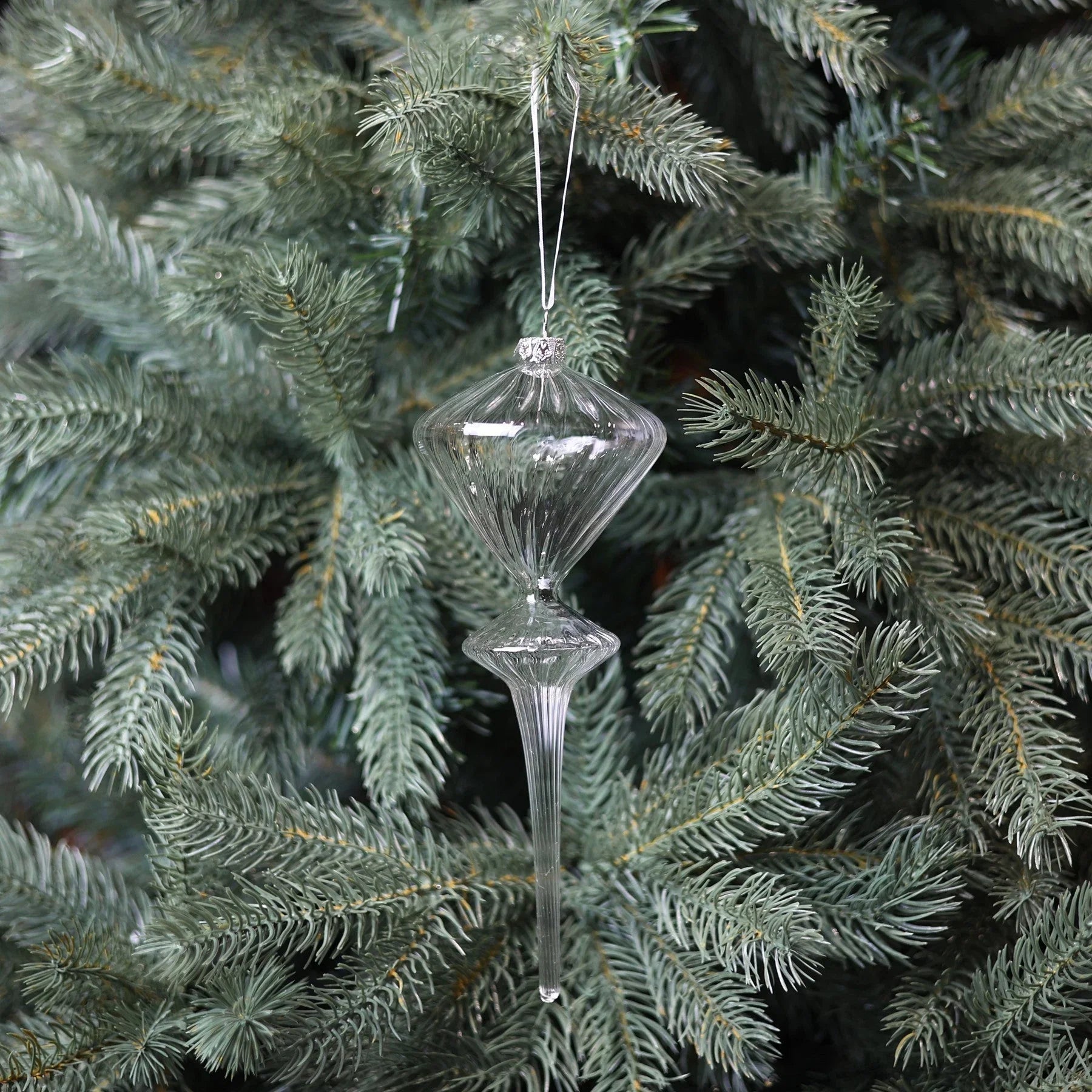 Clear glass ornament hanging on a pine Christmas tree branch, festive home decor