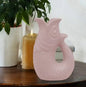 Pink fish-shaped decorative vase on wooden table with lit candle and potted plant