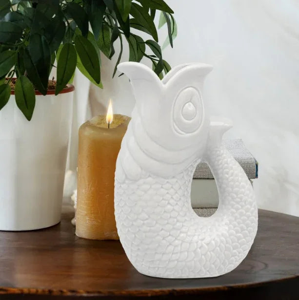 White ceramic fish sculpture on wooden table with plant and candle, modern home décor accent