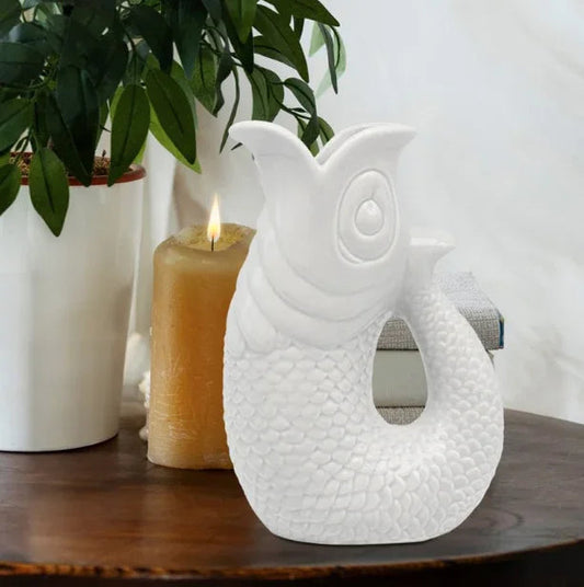 White ceramic fish sculpture on wooden table with plant and candle, modern home décor accent
