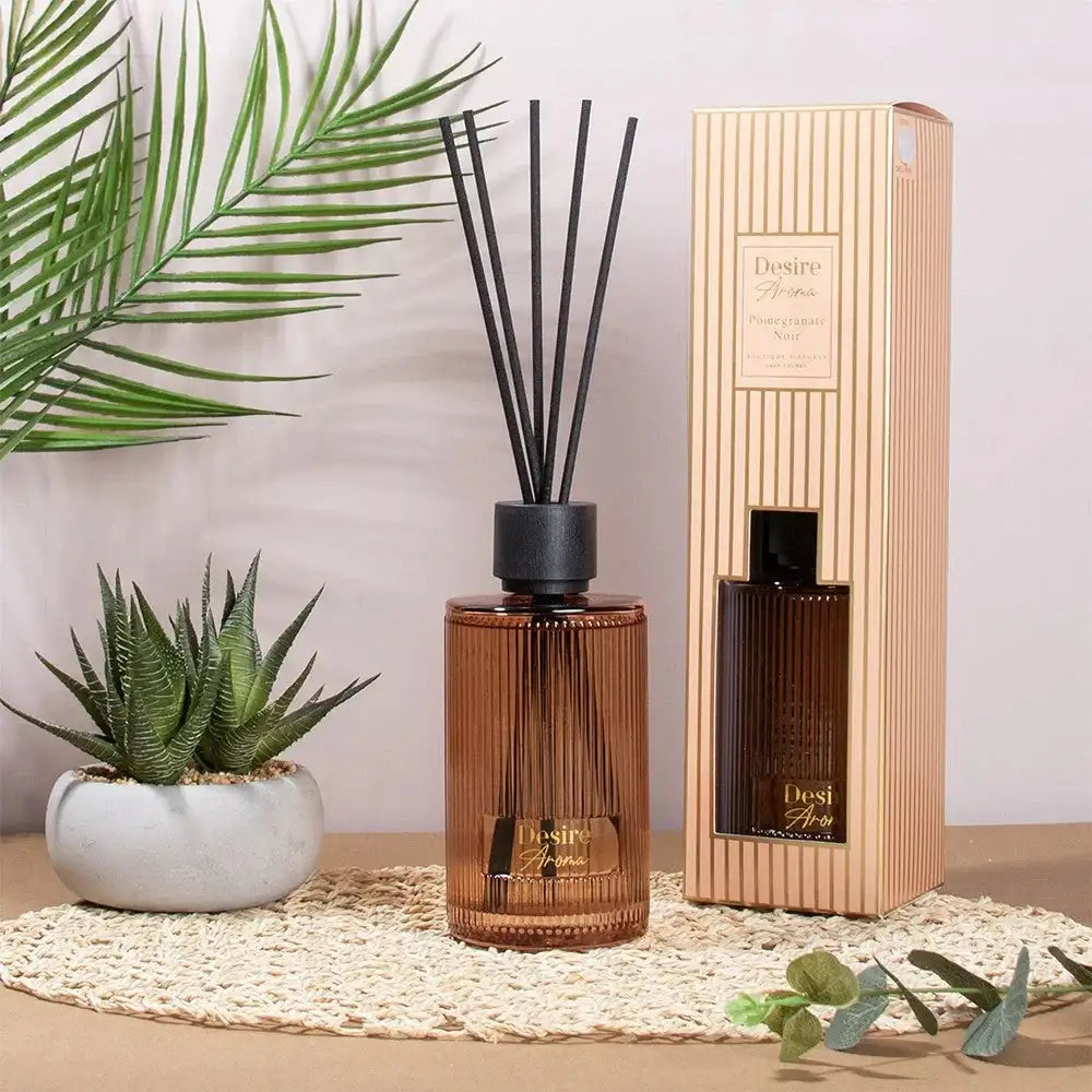 Brown glass reed diffuser with black sticks and gift box, surrounded by indoor plants, home decor.