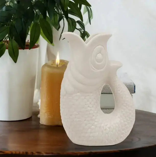 White ceramic fish figurine on wooden table with candle and plant, home decor accent