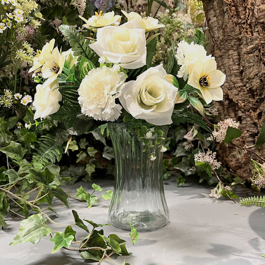 Artificial white roses and flowers in a glass vase, home décor, surrounded by greenery