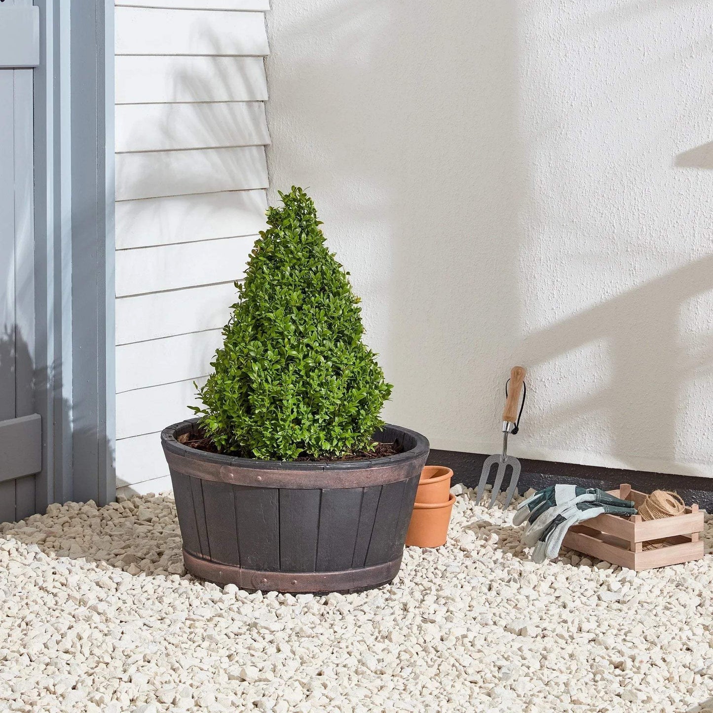 Outdoor artificial topiary bush in wooden planter with gardening tools and gloves on gravel