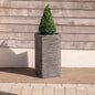 Tall textured planter with a cone-shaped topiary against a wooden wall, outdoor decor