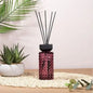 Purple glass reed diffuser with black sticks, displayed on a table with decorative plants