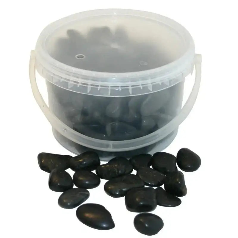 Bucket of smooth black decorative stones for home décor, with some stones scattered in front.