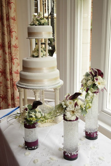 Elegant three-tier white wedding cake with cream ribbon and fresh floral decorations on table.