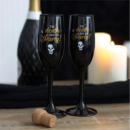 Black champagne flutes with skull design and 'Til Death Do Us Party' text, candles in background.